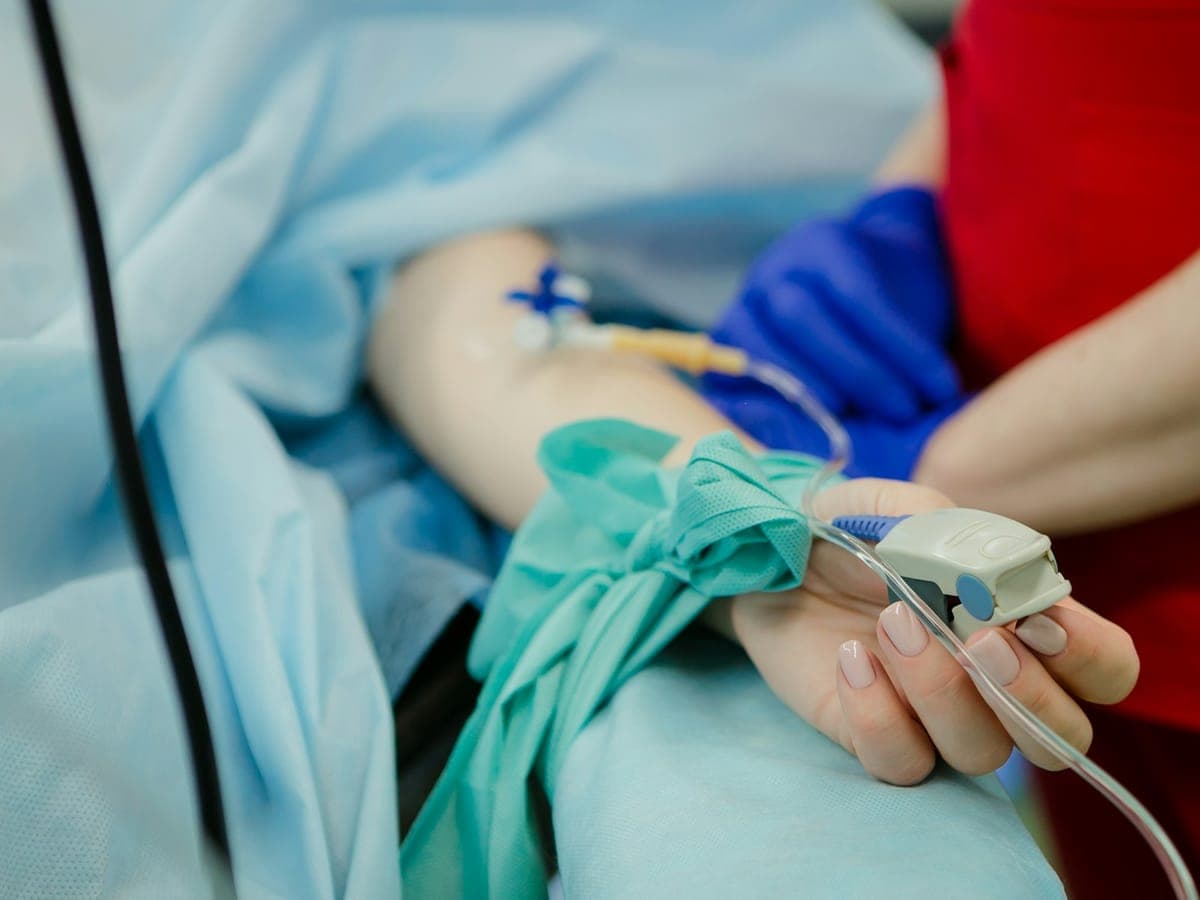 Patient's hand with a pulse oximeter, with someone sitting beside the bed