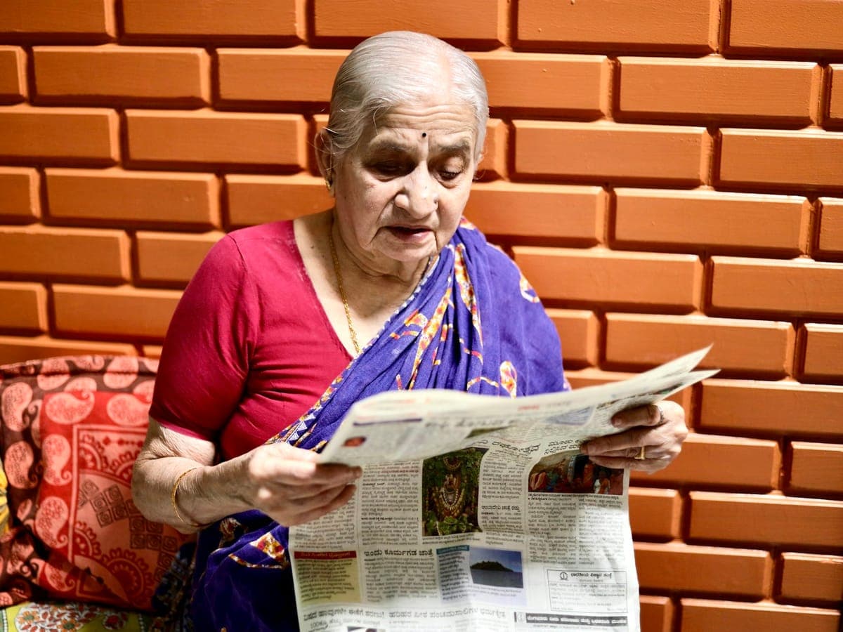 Elderly woman in a sari reading the newspaper at home