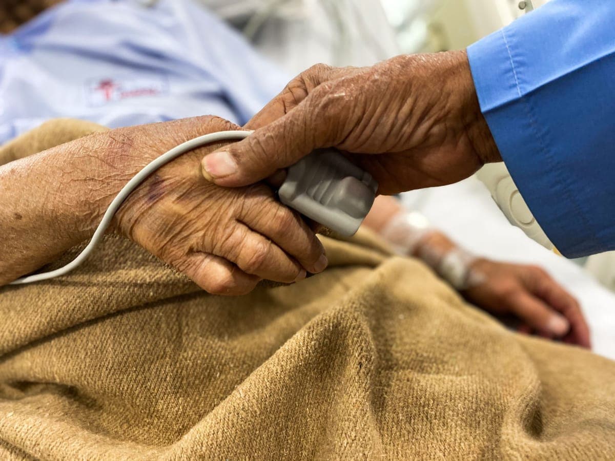 Family member holding an elderly patient's hand in a hospital bed